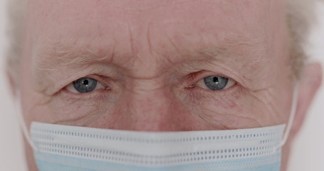 Macro portrait of wrinkled senior man with mask blinks into the camera
