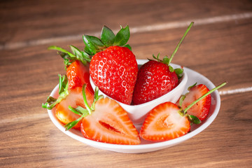 large fresh strawberries on a white ceramic plate and many sliced strawberries around the plate
