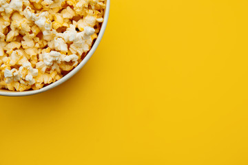 Popcorn in a bowl on yellow background, top view. Entetainement concept.