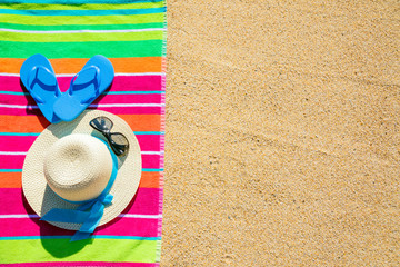 Beach towel with hat, sunglasses and flip flops photographed from above on sandy beach, hot summer...