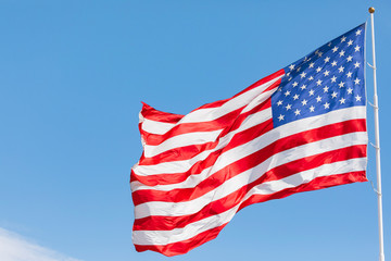 American flag waving in the wind on blue sky, US flag motion close-up, red white blue flag outdoors in sunlight. United States of America national flag. USA stars and stripes