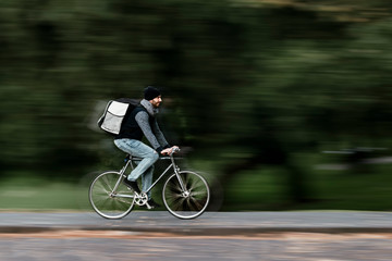 Food delivery courier riding fast in a motion blur background due to his high speed