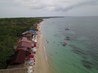 Fototapeta premium Aerial side view of Playa Blanca, with some boats, trees and restaurants, Baru Island, Colombia