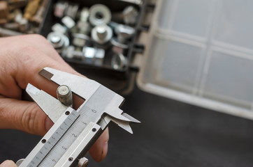 A male hand with a caliper measures the diameter of a bolt.