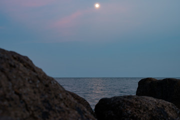 Fototapeta na wymiar Full moon at spectacular sunset over rocks and sea