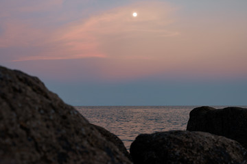 Obraz premium Full moon at spectacular sunset over rocks and sea