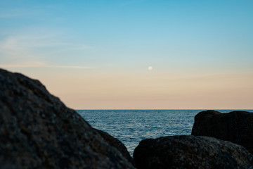 Fototapeta premium Full moon at spectacular sunset over rocks and sea