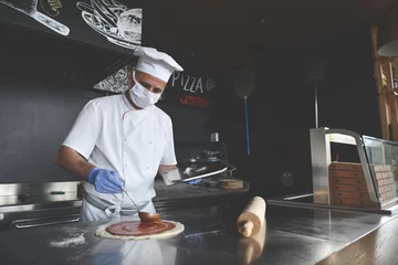 Selbstklebende Fototapeten chef  with protective coronavirus face mask preparing pizza © .shock