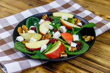Autumn spinach salad with apple, feta cheese, walnut and dried cranberry on wooden table. Healthy vegetarian food