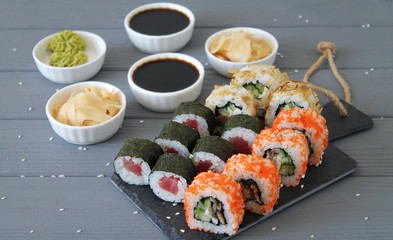 Various kinds of sushi rolls served on black stone and on gray wooden table