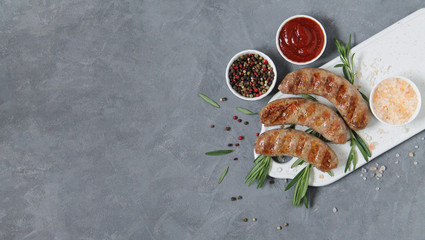 Grilled or fried sausages with sauce, spices, pink salt and rosemary on dark stone background