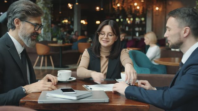 Men in suits are signing contract then shaking hands talking in restaurant with female translator. Agreements, communication and foreign contacts concept.