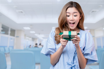 Fototapeta premium happiness cheerful asian female patient or sick woman in hospital uniform smile and hand hold gift box with ribbon smile facial expression insurance support and promotion takecare health ideas concept