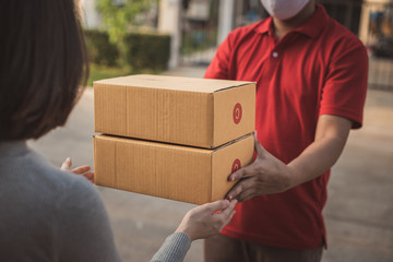 Deliver man wearing face mask in red uniform handling bag and  parcel box give to female costumer Postman and express grocery delivery service during covid19.