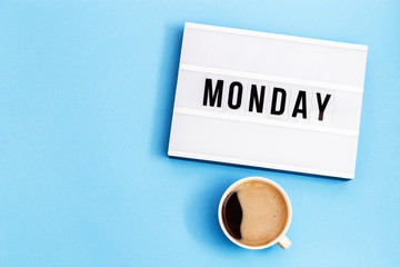Text "monday" on lightbox and cup of coffee for holiday - Thank God It’s Monday. Start of working week concept. Top view on blue background.
