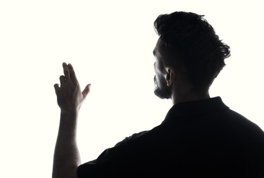 Silhouette of male person touches empty space with hand , back view back lit over white