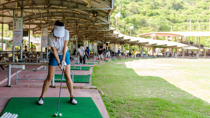 Healthy Sport.  Asian sporty woman swing golf ball practice at golf driving range on evening on...