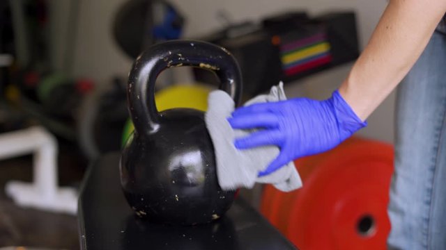 Woman disinfecting weight equipment in a gym because of coronavirus and reopening