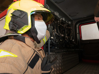 Firefighter getting on the truck equipped with an intervention suit, helmet and mask to protect...