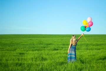 Girl with balloons in the field. Solar and positive energy of nature. Young beautiful woman on the grass in the Park.