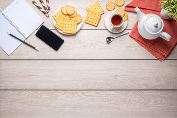 Afternoon tea set with bread, crackers, and a mobile phone and a notebook beside on the wooden table, with copy space, top view.