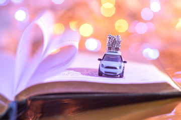 the car carries a box with a gift on the background of book pages. golden christmas lights. heart on a bright background. closeup of jewelry. silver jewelry 