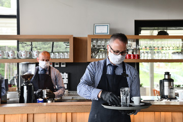 waiter in a medical protective mask serves  the coffee in restaurant