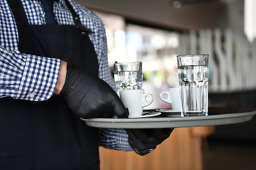 waiter in a medical protective mask serves  the coffee in restaurant