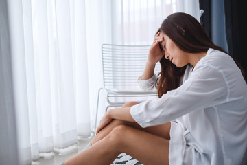 A sad and stressed young asian woman sitting alone in bedroom