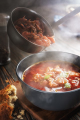 Borsch is poured into a bowl from a ladle from which steam, a traditional Ukrainian vegetable soup made from beets, carrots, tomatoes, potatoes, cabbage, herbs and garlic, close-up, shallow depth of