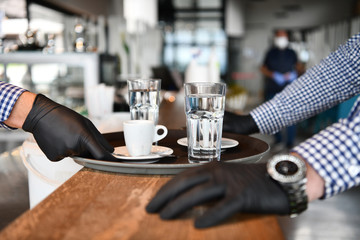 waiter in a medical protective mask serves  the coffee in restaurant