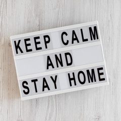 'Keep Calm and Stay Home' words on a modern board on a white wooden background, top view. Overhead, from above, flat lay.
