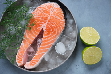 Round grey plate with raw iced salmon steak, fresh dill and lime. Above view on a grey concrete surface, horizontal shot