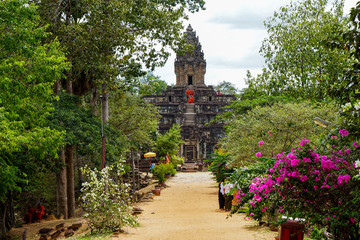 Siem Reap, Cambodia, July 17, 2019: 
Bakong temple, during the religious holiday, monks in orange robes walk through the ruins, horizontal photo, temple on the background of flowering trees          