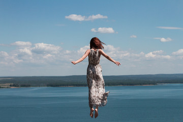 beautiful girl flies in a jump dressed in a dress against the blue sky