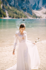 Fototapeta na wymiar Beautiful bride in a white chiffon dress with sleeves and lace on the shore of Lake Lago di Braies in Italy. Destination wedding in Europe, on the popular Braies lake.