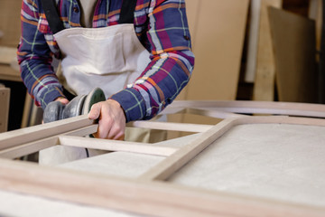 Hands of an unidentified young male carpenter grind wooden product. Concept of laborious work and men in wood production. Concept of handmade of own production