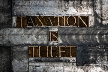 Photo of real authentic typeset letters forming Taxation Is Theft text on vintage textured grunge copper and silver background