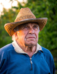 Fototapeta premium Elderly man in a straw hat on the background of the evening summer garden