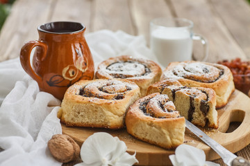 Basket of homemade buns with jam, served on old wooden table with walnuts and cup of milk