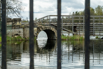Fototapeta na wymiar View of the park through the iron bars. The lake, the bridge. Daytime.