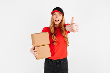 courier girl in uniform holding cardboard boxes and showing a thumbs up gesture on a white background. The concept of home delivery