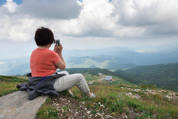 Naklejka na ściany i meble Senior woman taking photos with smartphone on the mountain