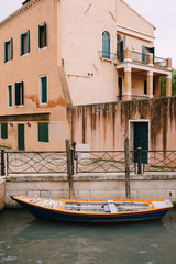 Fototapeta na wymiar Boats moored at the walls of a building in a canal in Venice, Italy. Classic Venetian street views - wooden shutters, brick houses, bridges