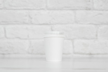 white paper cup on a white table against a white brick wall