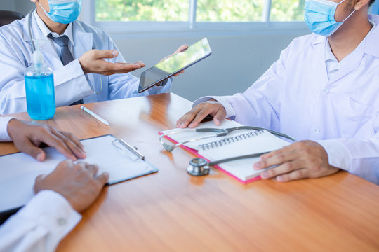 Asian medical team wearing medical masks technology network team meeting concept. Doctor at a table discussing a patients records working, Online medical treatment, New normal - Powered by Adobe