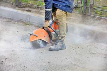 A construction worker using a portable gasoline saw cuts old asphalt to repair a site on the road. © Sergii