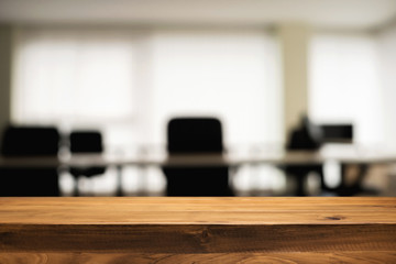 Empty wooden desk space over blurred office or meeting room background. Product display.