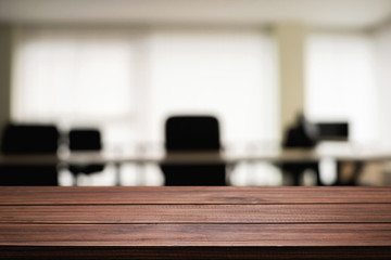 Empty wooden desk space over blurred office or meeting room background. Product display.