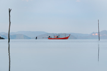Long tail boat and fisherman in a sea bay with calm water on a background of mountains at sunrise in summer